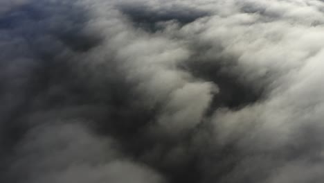 Flying-over-bright-white-clouds-and-dark-mysterious-land-in-shadow-below