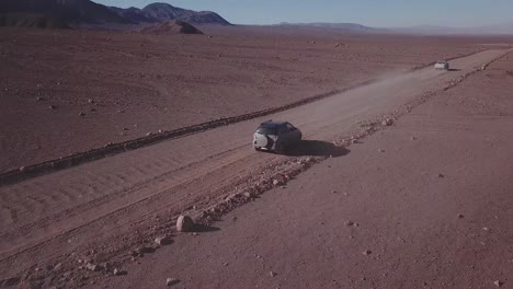 Two-cars-driving-on-a-dusty-road-in-the-Atacama-Desert-with-an-arid-landscape-in-Northern-Chile,-South-America
