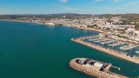 Drone-captures-charming-port-town-in-sunny-weather-with-a-beautiful-blue-sea-coast-backdrop