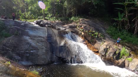 High-angle-shot-over-locals-bathing-in-Mo-Pang-Waterfall-surrounded-by-green-vegetation-in-Mae-Na-Toeng,-Pai-District,-Mae-Hong-Son,-Thailand-on-a-sunny-day