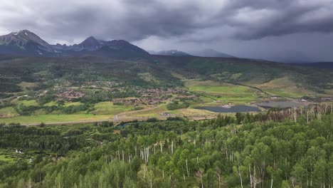 descending-on-a-lush-green-forest-of-aspen-trees-with-jagged-moody-mountains-in-the-background-in-silverthorne-colorado-AERIAL-DOLLY-DROP