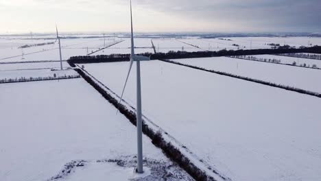 Flying-around-wind-turbine-rotating-blade-in-white-winter-landscape