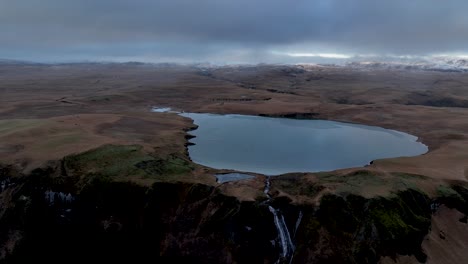 Cascada-De-Systrafoss-Y-Lago-Systravatn,-Contra-El-Cielo-Nublado-En-Islandia---Retroceso-Aéreo