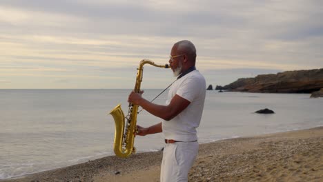 Wide-shot-of-senior-african-male-playing-the-saxophone-on-the-beach-during-golden-hour