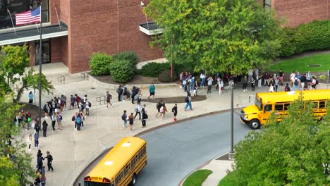 American-flag-and-yellow-school-bus-arriving-at-public-school-campus-with-large-group-of-students
