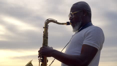 Nahaufnahme-Eines-Porträts-Eines-älteren-Afrikanischen-Mannes,-Der-Bei-Sonnenuntergang-Am-Strand-Saxophon-Spielt