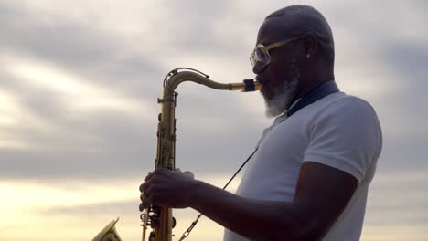 Primer-Plano-Retrato-De-Un-Anciano-Africano-Tocando-El-Saxofón-En-La-Playa-Durante-La-Puesta-De-Sol