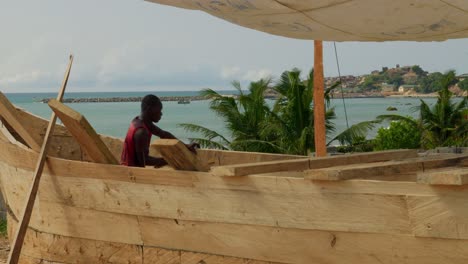 Black-african-carpenter-working-on-new-wooden-boat-with-hammer,-Ghana