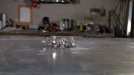 A-hand-full-of-M10-nut-falling-on-a-metal-table-in-super-slow-motion