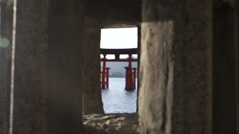 Cinematic-Shot-Looking-Through-Stone-Lantern-At-Floating-Grand-Torii-Gate-At-Itsukushima-Shrine
