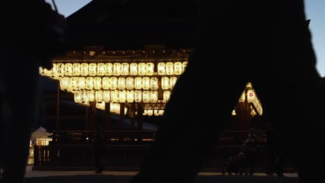 Silhouette-Of-People-Walking-Past-Illuminated-Hanging-Paper-Lanterns-At-The-Buden-Stage-In-Yasaka-Shrine,-Kyoto