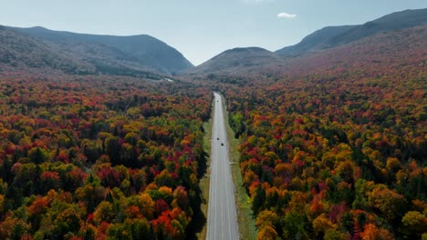 Centered-road-views-as-cars-passing-by-surrounded-with-fall-foliage-in-New-Hampshire-from-an-aerial-view