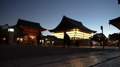 Silhouette-Of-People-Walking-Past-Illuminated-Hanging-Paper-Lanterns-At-The-Buden-Stage-And-South-Tower-Gate-At-Yasaka-Shrine,-Kyoto-In-The-Evening