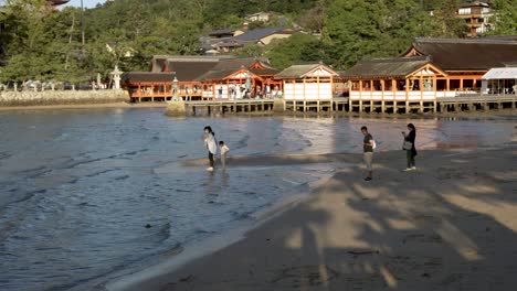 Se-Ve-A-Una-Familia-Vadeando-Las-Aguas-De-La-Marea-Entrante-En-El-Santuario-Itsukushima-Durante-La-Tarde