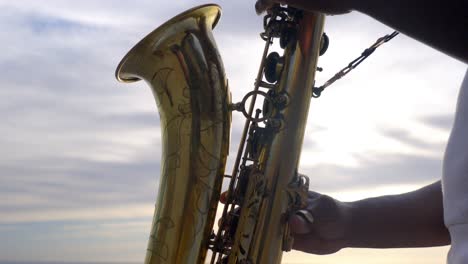 Nahaufnahme-Des-Saxophons,-Während-Es-Bei-Sonnenuntergang-Von-Einem-Musiker-Am-Strand-Gespielt-Wird