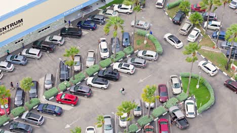 Drone-orbit-around-people-looking-for-parking-in-tropical-island-supermarket-lot