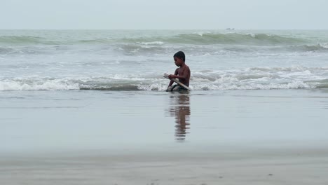 Ein-Kleiner-Junge-Spielt-Im-Meerwasser,-Während-Zwei-Menschen-Am-Strand-Vorbeigehen