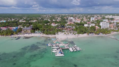 Luftaufnahme-Des-Sandigen-Strandes-Von-Boca-Chica-Mit-Steg-Und-Anlegenden-Booten-In-Der-Stadt-Santo-Domingo-An-Einem-Sonnigen-Tag