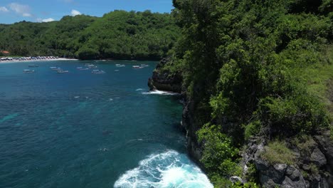A-lonely-island-off-the-coast-of-Nusa-Penida-with-a-rocky-arch-and-greenery-with-blue-crashing-waves,-aerial
