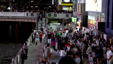 Multitudes-De-Personas-Iluminadas-Por-Carteles-De-Neón-Tomando-Fotos-Del-Hombre-De-Glico-Junto-Al-Canal-Dotonbori-Por-La-Noche