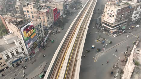 Aerial-drone-bird's-eye-shot-over-orange-line-train-near-McLeod-Road,-Lahore,-Pakistan-on-a-foggy-morning