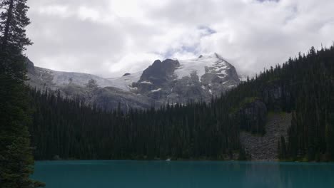Joffre-Lakes,-Pemberton,-British-Columbia,-Canada---A-Sight-of-a-Serene-Blue-Lake-Embraced-by-Lush-Greenery,-With-a-Snow-capped-Mountain-Gracing-the-Background---Wide-Shot