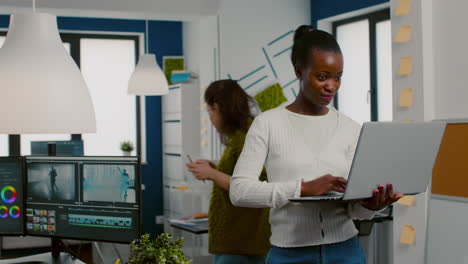 African-videographer-raising-head-smiling-at-camera-after-typing-at-laptop