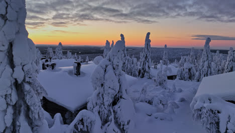 Aerial-close-up-shot-in-front-of-cottages-and-snowy-trees,-winter-dawn-in-Lapland