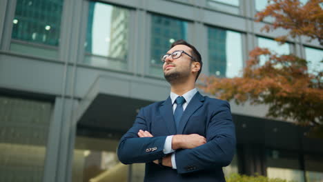 Confident-business-man-standing-in-front-of-office-building,-arms-crossed-looking-up-with-admiration