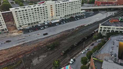 Aerial-top-down-shot-of-slowly-riding-cargo-train-in-city-of-Atlanta-Town-during-daytime,-America