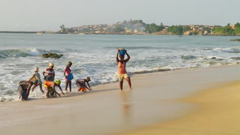 Mujeres-Africanas-Reuniendo-Y-Cargando-Arena-En-La-Playa-En-Grandes-Olas-Del-Mar