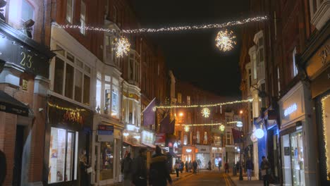 Gente-Caminando-Por-La-Calle-Comercial-Decorada-Con-Luces-Navideñas-Y-Adornos-Por-La-Noche-En-Dublín,-Irlanda