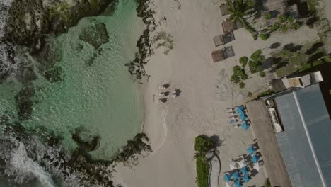 Descending-aerial-view-pointing-onto-beach-resort-area,-location-Caleta-Tankah,-beautiful-inlet-or-cove-in-the-Riviera-Maya-that-often-has-clear-water-when-other-beaches-have-seaweed