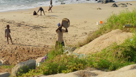 Mujer-Africana-Vaciando-Un-Balde-De-Arena-En-La-Playa,-Niños-Jugando