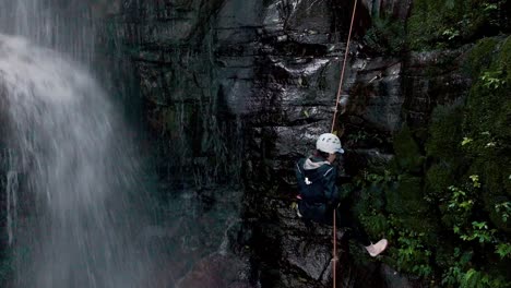 Luftaufnahme-Einer-Bergsteigerin,-Die-Neben-Dem-Wasserfall-Die-Steile-Bergwand-Hinuntergeht