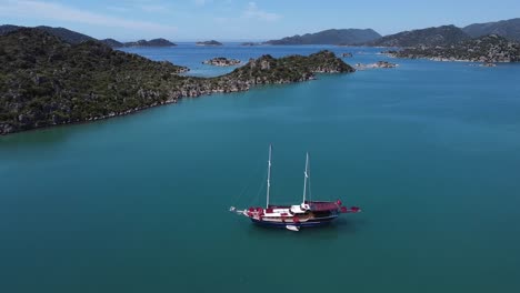 Aerial-view-of-sailboat-anchored-in-middle-of-bay-with-calm-blue-water-in-Aperlai-Ancient-City,-Turkey