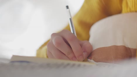 Close-up-of-womans-hand-lying-face-down-on-bed-writing-in-her-diary-with-pen