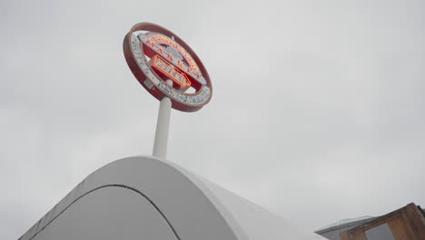 A-slow-left-to-right-orbiting-shot-captures-a-red-and-white-sign-reading-'Lonsdale-Quay-Market,'-framed-by-a-curved-cement-structure-in-the-foreground