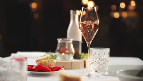 Fine-Dining-Szene-Mit-Brot-Und-Rosenblättern,-Blumen-In-Champagner-Schweben-An-Der-Oberfläche,-Bokeh-Hintergrund