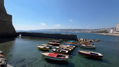 Serene-harbor-scene-with-a-variety-of-small-boats-moored-beside-a-sea-wall---Near-Castel-del-Ovo---Naples,-Italy