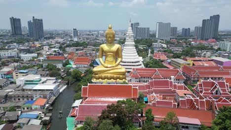 A-buddha-temple-statue-with-skyscrapers-behind-and-river-running-on-the-side-in-Bangkok,-Thailand