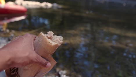 Hand-Holding-Half-Eaten-Sandwich-Over-Stream-While-Camping