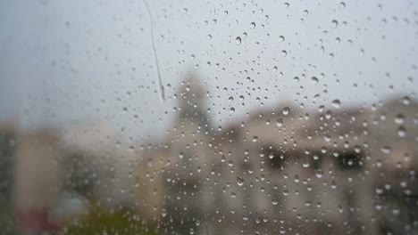 A-view-of-slow-motion-close-up-view-of-heavy-rain-as-raindrops-land-on-a-window-glass,-with-an-urban-city-landscape-in-the-background
