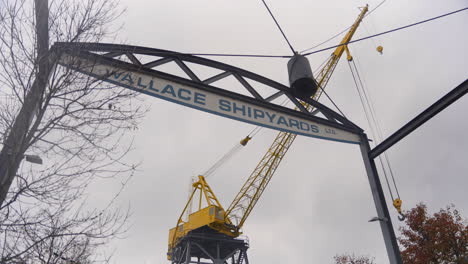 An-upward-tilt-to-reveal-the-Wallace-Shipyards-sign,-a-vibrant-yellow-crane-in-the-backdrop