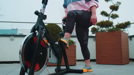 Chica-Atlética-Realizando-Ejercicios-De-Entrenamiento-Aeróbico-En-Bicicleta-Estática-En-El-Techo-De-La-Casa