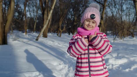 Una-Niña-Pequeña-Y-Alegre-Sonriendo,-Mostrando-Un-Gesto-De-Aprobación-En-Una-Carretera-Nevada-En-Un-Parque-De-Invierno-Al-Aire-Libre