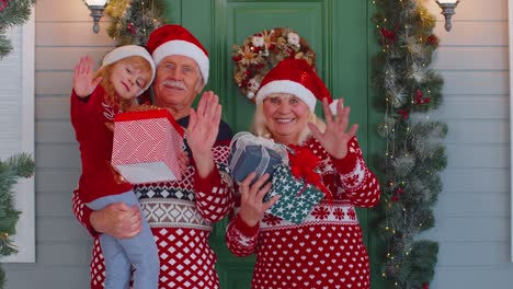 Ältere-Großmutter,-Großvater-Und-Enkelin-Stehen-Auf-Der-Veranda-Des-Weihnachtshauses-Und-Winken-Hallo