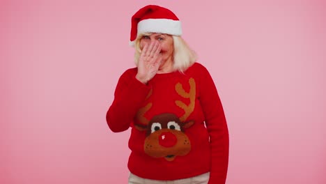 Grandmother-woman-in-Christmas-sweater-with-deers-waves-hand-palm-in-hello-gesture-welcomes-someone