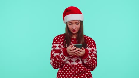 Una-Adolescente-Adulta-Con-Un-Suéter-Navideño-Mirando-La-Pantalla-Del-Teléfono-Inteligente-Regocijándose-Sinceramente-Por-Ganar-éxito-Y-Suerte