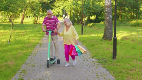 Senior-stylish-couple-grandmother,-grandfather-after-shopping-with-bags-using-scooter-for-riding